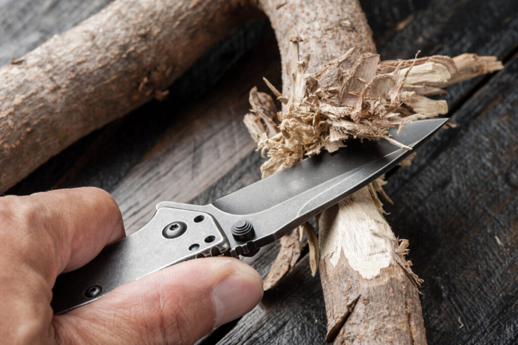 Man cutting tree branch with hunting knife