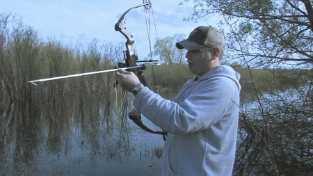 Bowfisher fixing arrow in a shruby lake