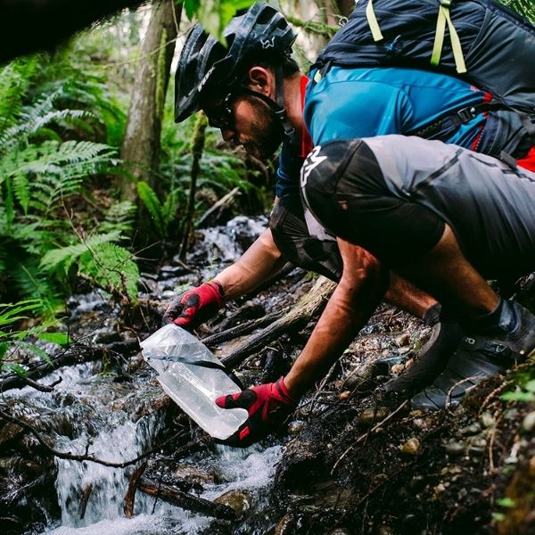 Hiker filling platypus reservoir with stream water