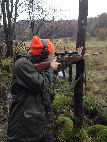 Hunter aiming rifle by the tree during fall