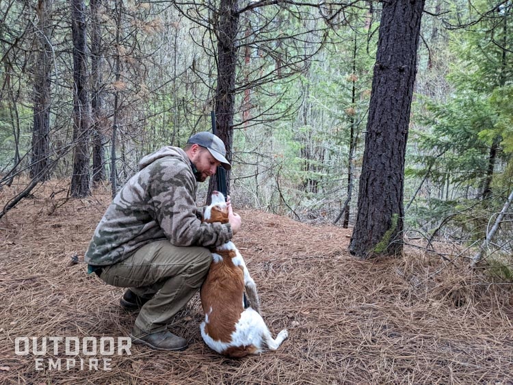 Hunter crouching down with dog in forest