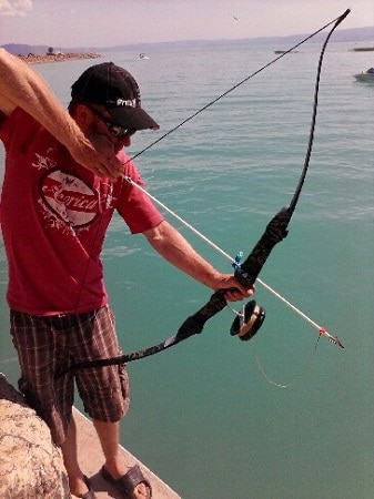 Man bowfishing with recurve on a cliff by the beach