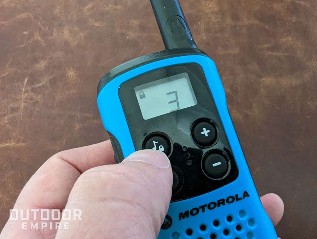 Thumb pressing the keypad lock button on a blue walkie talkie
