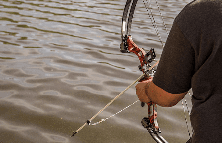 Bowfisher aiming his bow on water